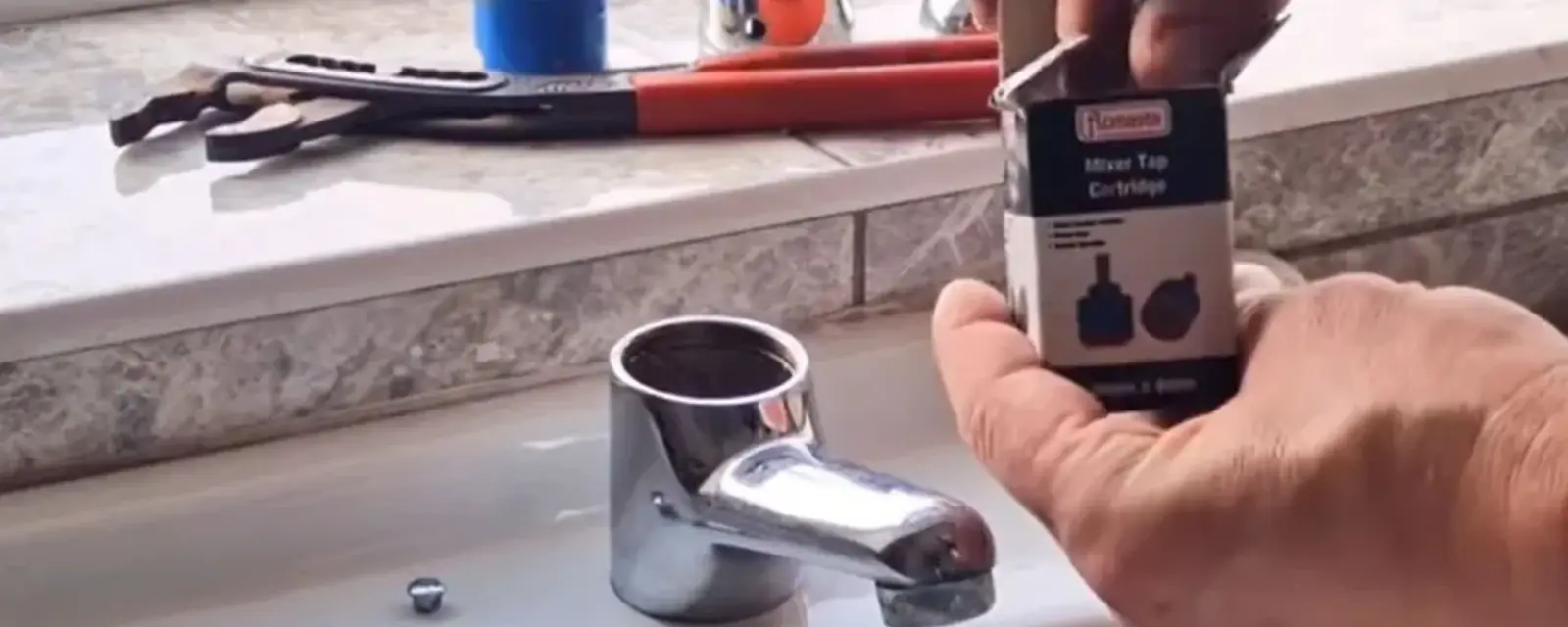 Hands holding a replacement faucet cartridge beside a bathroom sink