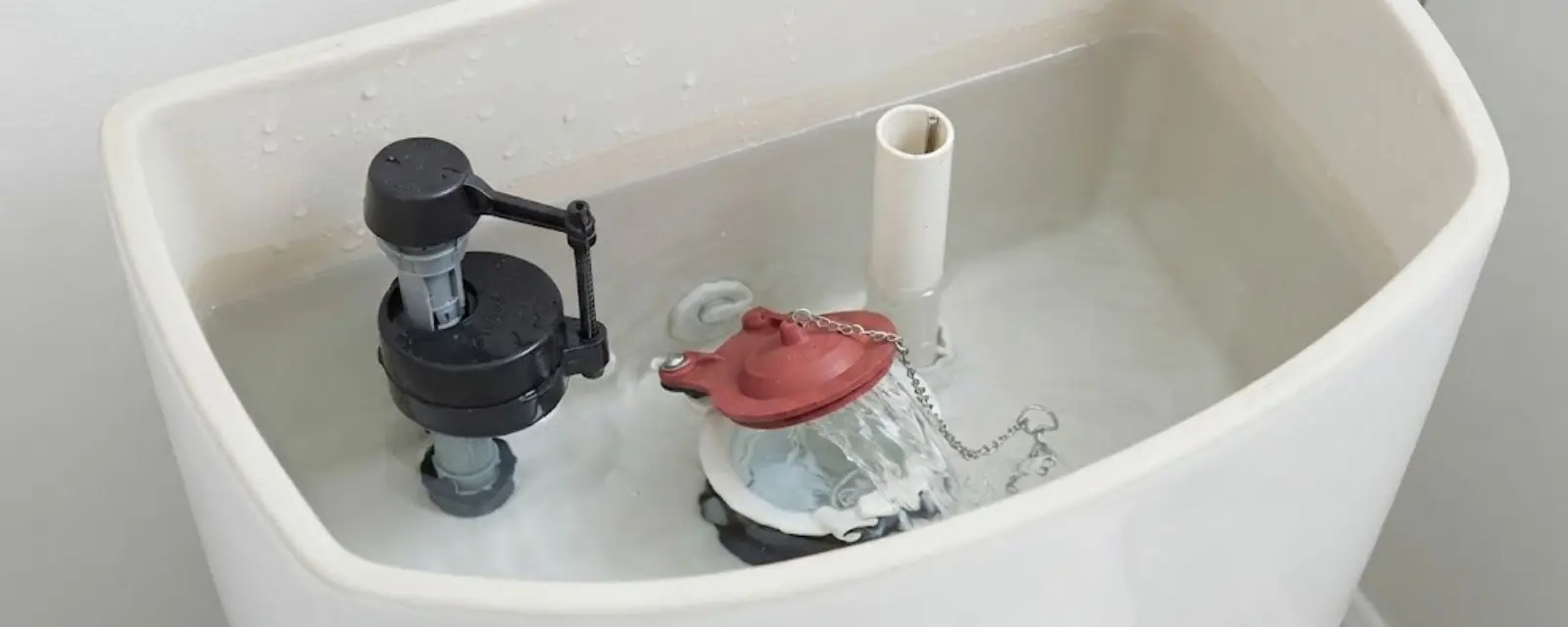 Inside of an open toilet tank showing the fill valve and flapper