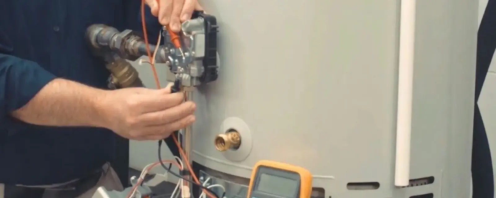 Hands testing the wiring of a residential water heater with a multimeter