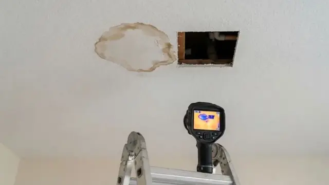 Thermal imaging camera pointed at a water-stained ceiling from a ladder