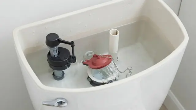 Inside of an open toilet tank showing the fill valve and flapper
